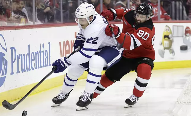 Toronto Maple Leafs defenseman Jake McCabe (22) controls the puck past New Jersey Devils left wing Tomas Tatar (90) during the second period of an NHL hockey game Thursday, Oct. 10, 2024, in Newark, N.J. (AP Photo/Adam Hunger)