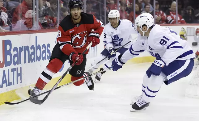 New Jersey Devils defenseman Johnathan Kovacevic (8) passes he puck past Toronto Maple Leafs center John Tavares (91) during the third period of an NHL hockey game Thursday, Oct. 10, 2024, in Newark, N.J. (AP Photo/Adam Hunger)