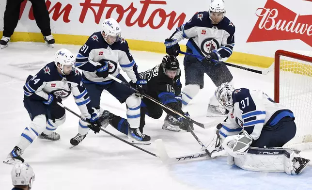 Toronto Maple Leafs' Mitch Marner (16) takes a shot on Winnipeg Jets' goaltender Connor Hellebuyck (37) as Josh Morrissey (44), Cole Perfetti (91) and Vladislav Namestnikov (7) defend during the first period of an NHL hockey game in Winnipeg, Manitoba, Monday, Oct. 28, 2024. (Fred Greenslade/The Canadian Press via AP)