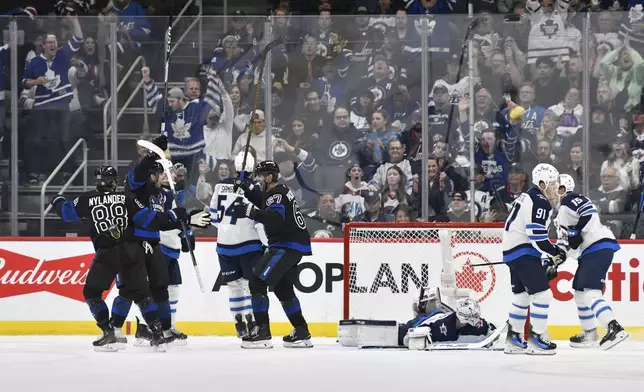 Toronto Maple Leafs' John Tavares, second from left, celebrates after his goal against Winnipeg Jets goaltender Connor Hellebuyck, third from right, with William Nylander (88) and Max Pacioretty (67) during second-period NHL hockey game action in Winnipeg, Manitoba, Monday, Oct. 28, 2024. (Fred Greenslade/The Canadian Press via AP)