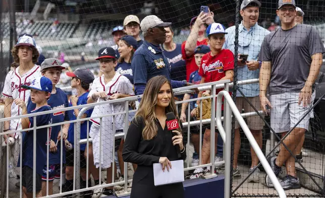 Bally reporter, Hanna Yates, broadcasts her pregame with fans standing behind her waiting for autographs before the start of a baseball game between the New York Mets and the Atlanta Braves, Monday, Sept. 30, 2024, in Atlanta. (AP Photo/Jason Allen)