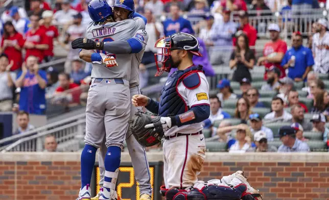 New York Mets' Francisco Lindor, left, and Starling Marte, center, celebrate at home plate after scoring in the ninth inning of a baseball game against the Atlanta Braves, Monday, Sept. 30, 2024, in Atlanta. (AP Photo/Jason Allen)