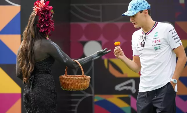 Mercedes driver George Russell of Britain receives a flower from a model dressed as "catrina" as he arrives to the Hermanos Rodriguez racetrack ahead of the Formula One Mexico Grand Prix auto race in Mexico City, Thursday, Oct. 24, 2024. (AP Photo/Moises Castillo)