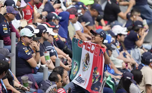 A fan of Red Bull driver Sergio Perez poses for photos with a Mexican flag during the third free practice ahead of the Formula One Mexico Grand Prix auto race at the Hermanos Rodriguez racetrack in Mexico City, Saturday, Oct. 26, 2024. (AP Photo/Eduardo Verdugo)