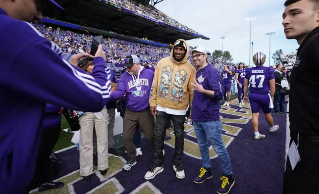 Former Washington quarterback Michael Penix Jr., in gold, takes photos with fans before an NCAA college football game against Michigan, Saturday, Oct. 5, 2024, in Seattle. (AP Photo/Lindsey Wasson)