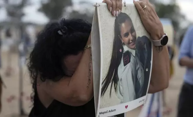 A woman leans on a picture of Mapal Adam, at the site of the Nova music festival, where hundreds of revelers were killed and abducted by Hamas and taken into Gaza, on the one-year anniversary of the attack, near Kibbutz Reim, southern Israel, Monday, Oct. 7, 2024. (AP Photo/Ariel Schalit)