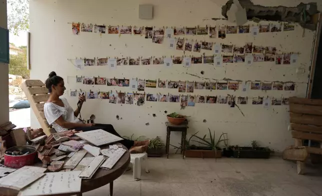 A woman sits next to a damaged wall where portraits of victims hang, as Israel marks the one-year anniversary of the Hamas attack on Israel, at the Kibbutz Be'eri, an Israeli communal farm on the Gaza border, on Monday, Oct. 7, 2024. (AP Photo/Ohad Zwigenberg)