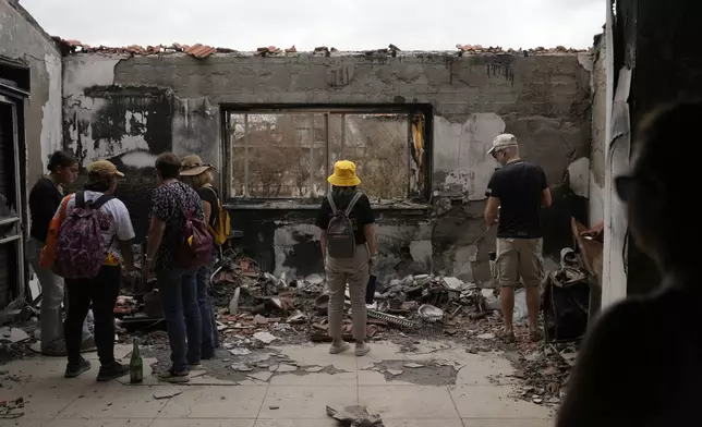 People stand at a battle-scarred home at the Kibbutz Be'eri, an Israeli communal farm on the Gaza border, as Israel marks the one-year anniversary of the Hamas attack on Israel on Monday, Oct. 7, 2024. (AP Photo/Ohad Zwigenberg)