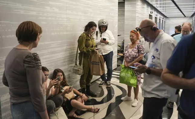 People take cover as a siren warns of incoming rockets fired from Yemen, in Ramat Gan, Israel, Monday, Oct. 7, 2024. (AP Photo/Oded Balilty)