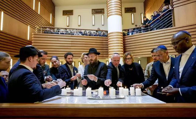 Survivor Alon Gat, Rabi Yehuda Teichtal and Berlin mayor Kai Wegner, centre from left, hold a candle-lighting ceremony marking the first anniversary of the Hamas spearheaded attacks on Israel, at the synagogue of the Chabad community in Berlin, Germany, Monday, Oct. 7, 2024. (AP Photo/Markus Schreiber)