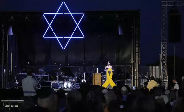 Survivor Michal Ohana speaks as members of the Jewish community wave electronic candles as they gather at a park in Sydney, Australia, on Monday, Oct. 7, 2024, as mourners marked the anniversary of the Oct. 7, 2023, attack in Israel. (AP Photo/Rick Rycroft)