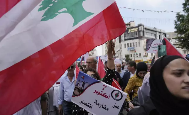 A Palestinian activist flies the Lebanon flag and holds a poster that reads "October 7th is dignity, resistance and victory," during a protest marking the one year anniversary of the Israel Hamas war, in the West Bank city of Ramallah, Monday, Oct. 7, 2024. (AP Photo/Nasser Nasser)