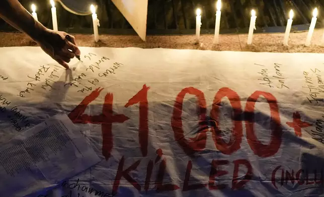 Activists light candles and write the names of Palestinian casualties on a banner as they hold a pro-Palestinian rally to mark the one-year anniversary of the Israel Hamas war on Monday Oct. 7, 2024, in Quezon City, Philippines. (AP Photo/Aaron Favila)