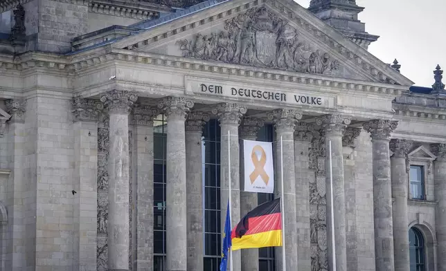 A commemorative ribbon with the inscription "October 7, 2023" hangs on the Reichstag building behind flags hanging at half-mast to mark the one-year anniversary of the Hamas attack in Israel, Monday, Oct. 7, 2024. (Kay Nietfeld/dpa/dpa via AP)