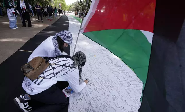 Two young women write on a giant flag as pro-Palestinian supporters rally in Sydney, Sunday, Oct. 6, 2024. (AP Photo/Rick Rycroft)