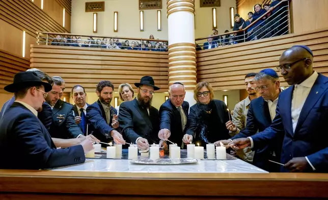 Survivor Alon Gat, Rabi Yehuda Teichtal and Berlin mayor Kai Wegner, centre from left, hold a candle-lighting ceremony marking the first anniversary of the Hamas spearheaded attacks on Israel, at the synagogue of the Chabad community in Berlin, Germany, Monday, Oct. 7, 2024. (AP Photo/Markus Schreiber)