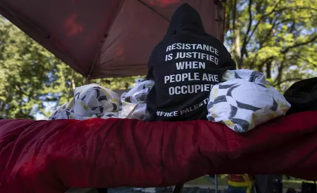 A protester sits on a cot on the side of the road near the driveway of Ohio Democratic Rep. Greg Landsman's Cincinnati residence wearing a sweatshirt that reads "Resistance is justified when people are occupied #Free Palestine," Monday, Oct. 7, 2024. (AP Photo/Carolyn Kaster)