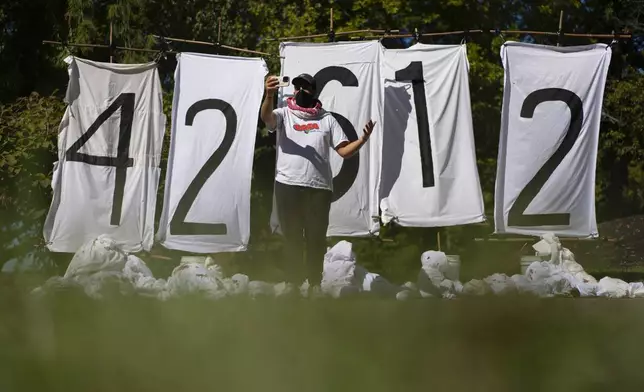 Mike Madanat speaks during a cell phone interview in front of a display of the number of people who have died in Gaza, near the driveway of Ohio Democratic Rep. Greg Landsman's Cincinnati residence, Monday, Oct. 7, 2024. (AP Photo/Carolyn Kaster)