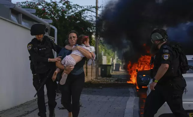 Police officers evacuate a woman and a child from a site hit by a rocket fired from the Gaza Strip, in Ashkelon, southern Israel, Saturday, Oct. 7, 2023. (AP Photo/Tsafrir Abayov)