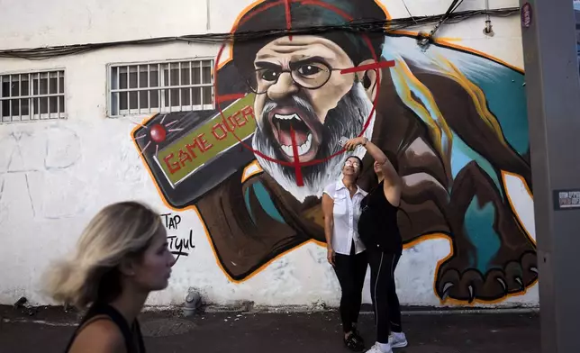 Two women take a selfie next to newly painted graffiti of Hezbollah leader Hassan Nasrallah a day after Hezbollah confirmed its leader was killed in an Israeli airstrike, in Tel Aviv, Israel, on Sunday, Sept. 29, 2024. (AP Photo/Oded Balilty)