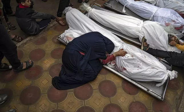 A woman mourns the covered bodies of her child and her husband killed in an Israeli army bombardment of the Gaza Strip, in the hospital in Khan Younis, Tuesday Dec. 5, 2023. (AP Photo/Fatima Shbair)