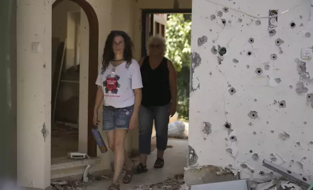 Liora Eilon, right, walks through her home that was destroyed by an Israeli tank on Oct. 7, with her daughter, Hadas Eilon-Carmi, left, in Kibbutz Kfar Aza, southern Israel, Sunday, Aug. 18, 2024. (AP Photo/Ohad Zwigenberg)