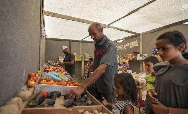 Ne'man Abu Jarad buys vegetables at a market inside a displacement camp, where he and his family now live after being displaced over five times since the start of the Israel-Hamas war, in Muwasi, Gaza Strip, Thursday, Sept. 12, 2024. (AP Photo/Abdel Kareem Hana)