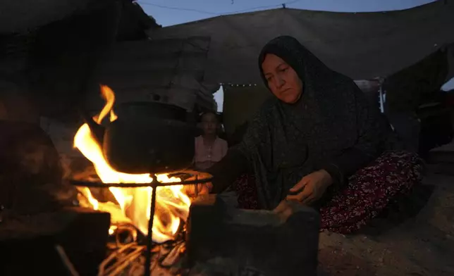 Shifa Hijo cooks on fire in a tent camp, where she and her family now live after being displaced over five times since the start of the Israel-Hamas war, in Muwasi, Gaza Strip, Sunday, Sept. 15, 2024. (AP Photo/Abdel Kareem Hana)