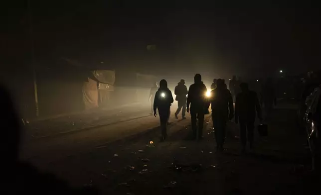 FILE - Palestinians displaced by the Israeli bombardment of the Gaza Strip walk in the dark with flashlights at the makeshift tent camp in the Muwasi area on Sunday, Dec. 31, 2023. (AP Photo/Fatima Shbair, File)