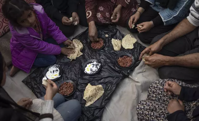 FILE - Members of the Abu Jarad family, who were displaced by the Israeli bombardment of the Gaza Strip, eat breakfast at a makeshift tent camp in the Muwasi area, southern Gaza, Monday, Jan. 1, 2024. (AP Photo/Fatima Shbair, File)