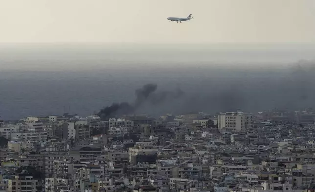 A Middle East Airlines airplane flies over Beirut as smoke rises from Israeli airstrikes in Dahiyeh, Beirut, Tuesday, Oct. 1, 2024. (AP Photo/Bilal Hussein)