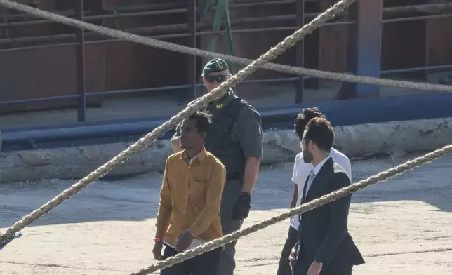 Migrants and security officials walk at the port of Shengjin, northwestern Albania. Wednesday, Oct. 16, 2024 after disembarking from the Italian navy ship Libra carrying the first group of 16 migrants intercepted in international waters. (AP Photo/Vlasov Sulaj)