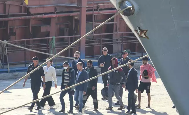 Migrantw and security officials walk at the port of Shengjin, northwestern Albania. Wednesday, Oct. 16, 2024 after disembarking from the Italian navy ship Libra, carrying the first group of 16 migrants intercepted in international waters. (AP Photo/Vlasov Sulaj)