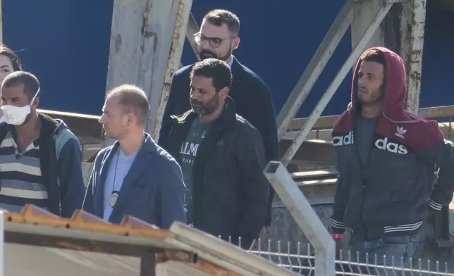 Migrants and security officials walk at the port of Shengjin, northwestern Albania. Wednesday, Oct. 16, 2024 after disembarking from the Italian navy ship Libra, carrying the first group of 16 migrants intercepted in international waters. (AP Photo/Vlasov Sulaj)