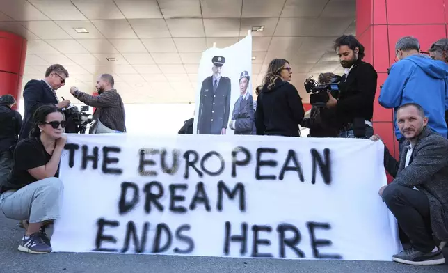 Activists, holding pictures of the Italian and Albanian premiers dressed as police officers, protest at the entrance of the port of Shengjin, northwestern Albania, Wednesday, Oct. 16, 2024, following the arrival of an Italian navy ship carrying the first group of migrants who were intercepted in international waters. (AP Photo/Vlasov Sulaj)