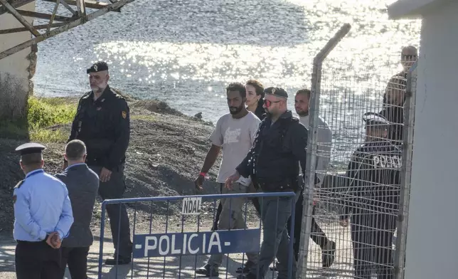 Migrants and security officials walk at the port of Shengjin, northwestern Albania. Wednesday, Oct. 16, 2024 after disembarking from the Italian navy ship Libra, carrying the first group of 16 migrants intercepted in international waters. (AP Photo/Vlasov Sulaj)