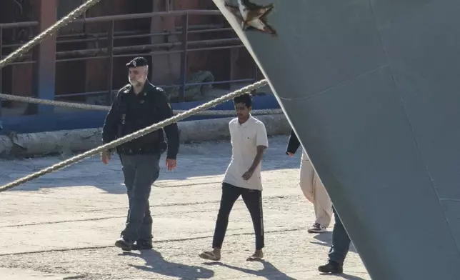 A migrant and security officials walk at the port of Shengjin, northwestern Albania. Wednesday, Oct. 16, 2024 after disembarking from the Italian navy ship Libra, carrying the first group of 16 migrants intercepted in international waters. (AP Photo/Vlasov Sulaj)