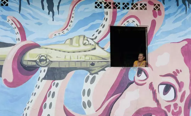 A resident is framed by the facade of her home emblazoned with a mural of an octopus, in Puerto Lopez, Ecuador, Tuesday, Sept. 24, 2024. (AP Photo/Dolores Ochoa)