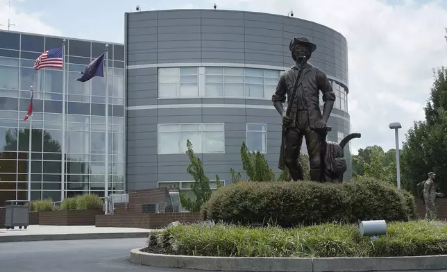 A soldier in camouflage, right, walks past the "Minute Man" statue outside the National Guard headquarters in Raleigh, N.C., on Tuesday, July 30, 2024. (AP Photo/Allen G. Breed)