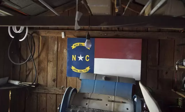 A wood panel painted with the North Carolina state flag hangs on the wall of a little barn behind Chris Arthur's home outside Mount Olive, N.C., on Monday, July 15, 2024. It was in this barn that the Army veteran spoke with a government informant, whose recording helped convict Arthur in federal court. (AP Photo/Allen G. Breed)