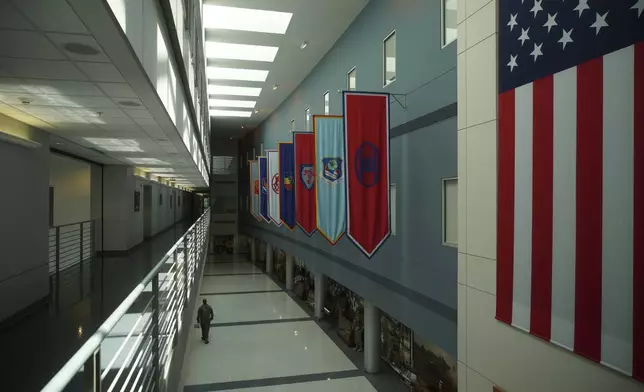 A soldier walks down a hall displaying unit flags at the National Guard headquarters in Raleigh, N.C., on Tuesday, July 30, 2024. Chris Arthur served with the 30th Armored Brigade Combat Team, whose banner is just to the left of the American flag. (AP Photo/Allen G. Breed)