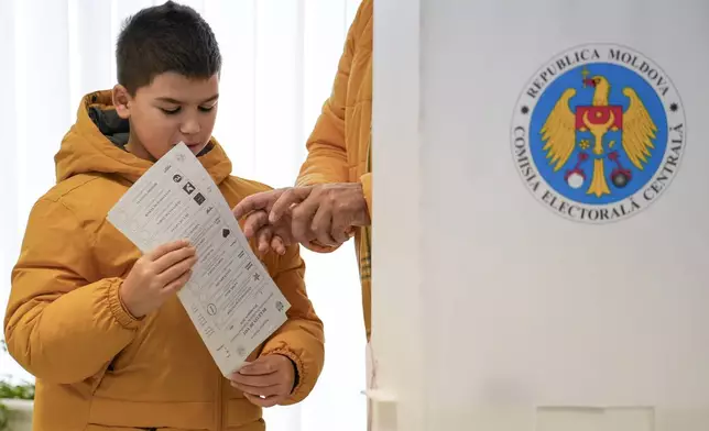 A child holds a voting ballot in Chisinau, Moldova, Sunday, Oct. 20, 2024, during a presidential election and a referendum on whether to enshrine in the Constitution the country's path to European Union membership. (AP Photo/Vadim Ghirda)