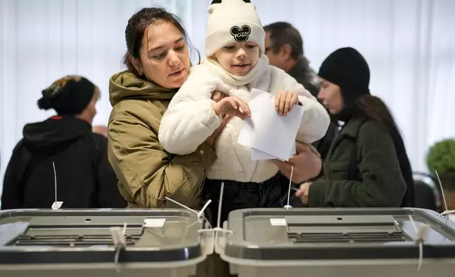 A woman holds a child as she casts her vote in Chisinau, Moldova, Sunday, Oct. 20, 2024, during a presidential election and a referendum on whether to enshrine in the Constitution the country's path to European Union membership. (AP Photo/Vadim Ghirda)