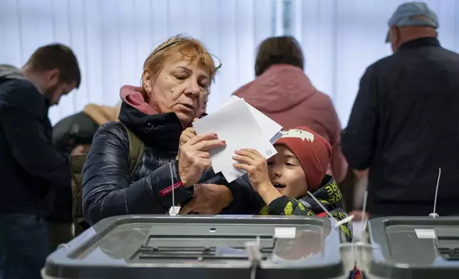 A woman hands a child her vote to cast in Chisinau, Moldova, Sunday, Oct. 20, 2024, during a presidential election and a referendum on whether to enshrine in the Constitution the country's path to European Union membership. (AP Photo/Vadim Ghirda)