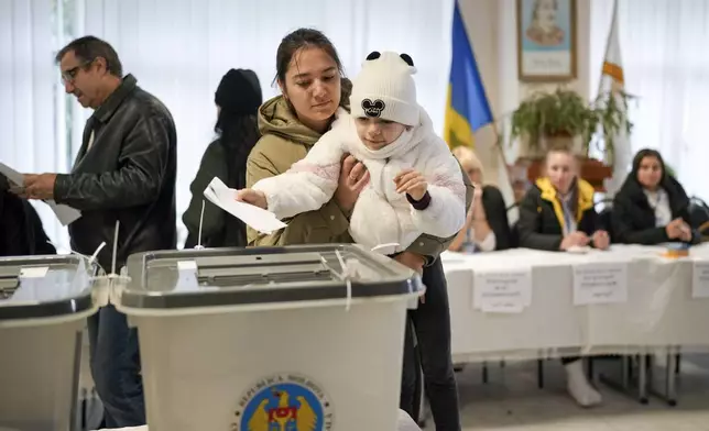 A woman holds a child as she casts her vote in Chisinau, Moldova, Sunday, Oct. 20, 2024, during a presidential election and a referendum on whether to enshrine in the Constitution the country's path to European Union membership. (AP Photo/Vadim Ghirda)