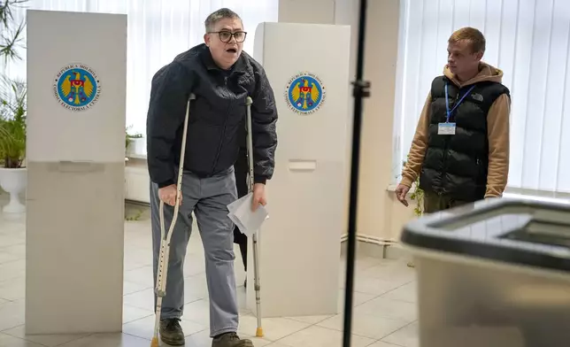 A man using crutches exits a voting booth in Chisinau, Moldova, Sunday, Oct. 20, 2024, during a presidential election and a referendum on whether to enshrine in the Constitution the country's path to European Union membership. (AP Photo/Vadim Ghirda)