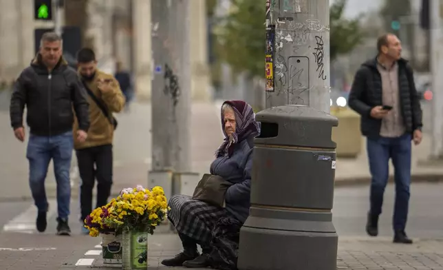 People walk by a woman selling flowers in Chisinau, Moldova, Thursday, Oct. 17, 2024, ahead of a presidential election and a referendum of whether to enshrine in Moldova's Constitution its path to European Union membership taking place on Oct.20. (AP Photo/Vadim Ghirda)