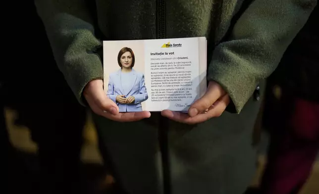 A girl holds a leaflet showing Moldova's President Maia Sandu while listening to her speaking to supporters in Magdacesti, Moldova, Thursday, Oct. 17, 2024, as she seeks a second term in office ahead of a presidential election and a referendum of whether to enshrine in Moldova's Constitution its path to European Union membership taking place on Oct.20. (AP Photo/Vadim Ghirda)