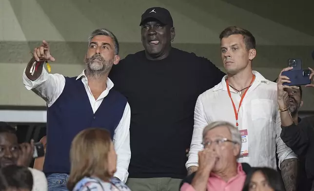 American former professional basketball player Michael Jordan, center, gestures as he attends the Champions League opening phase soccer match between Monaco and Barcelona at the Louis II stadium, in Monaco, Monaco, Thursday, Sept. 19, 2024. (AP Photo/Laurent Cipriani)