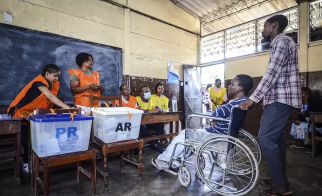 A woman in a wheelchair is helped at a polling station to vote in general elections in Maputo, Mozambique, Wednesday, Oct. 9, 2024. (AP Photo/Carlos Equeio)